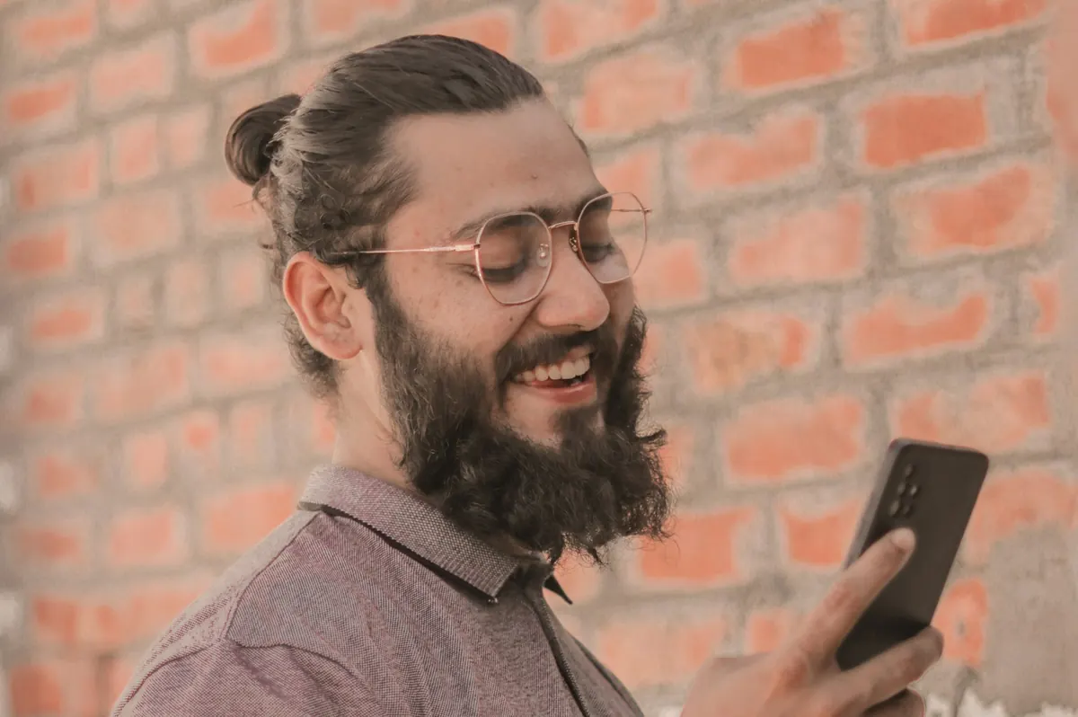 A smiling man with a beard reading a message on his phone